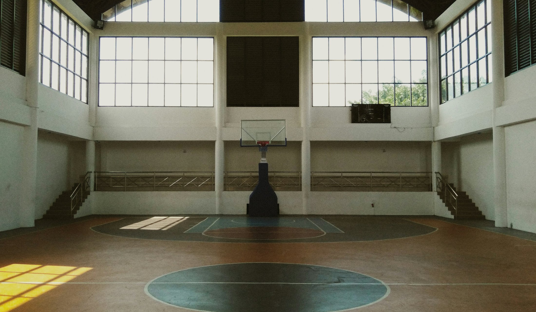 Indoor basketball court with sunlight through tall windows